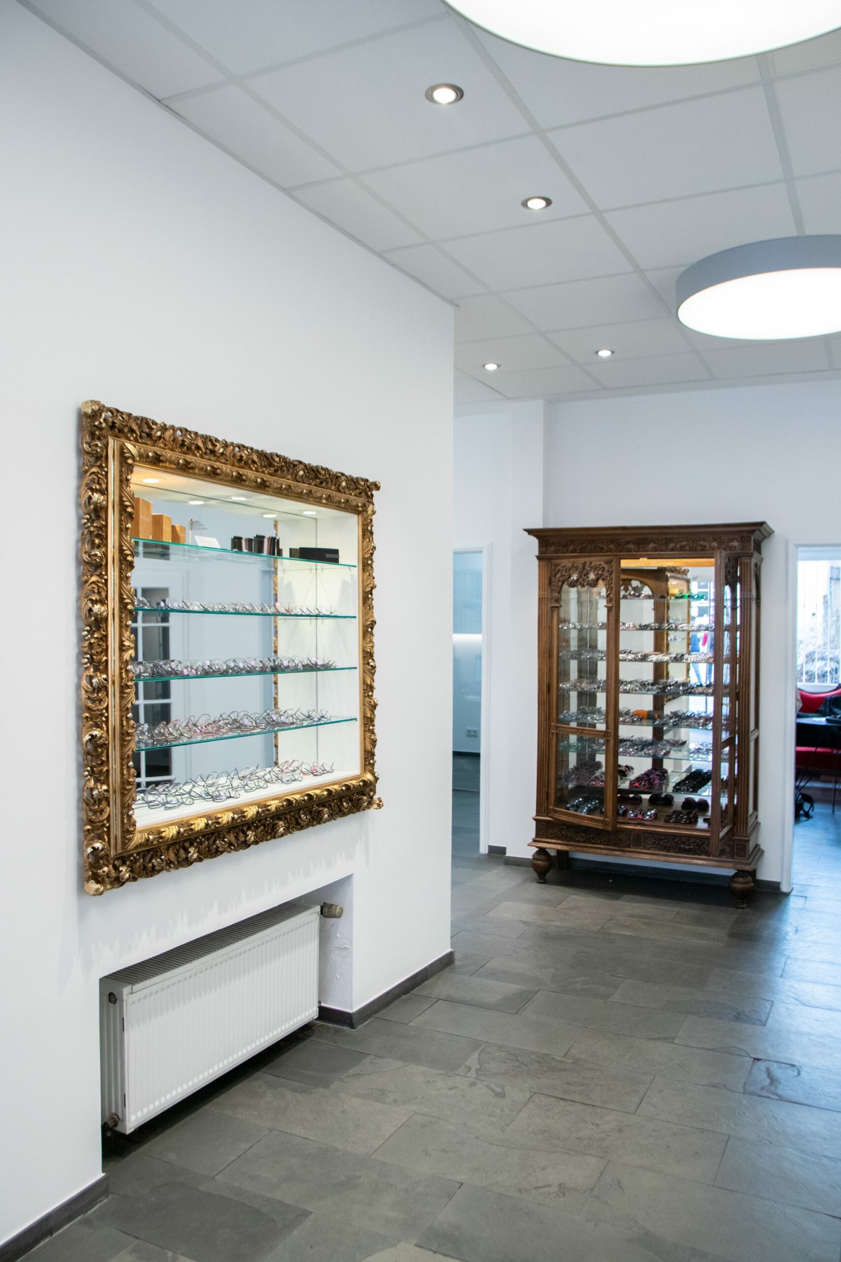 Das Bild zeigt den Verkaufsraum von die Brille Trier mit einem goldenen Spiegel an der Wand und einem Schrank im Hintergrund